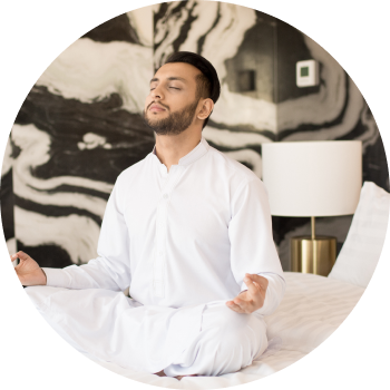 A man dressed in white sits cross-legged with eyes closed and meditating