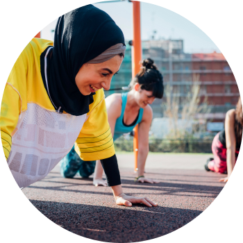 A smiling woman in black hijab and yellow t-shirt performs plank pose in outdoors